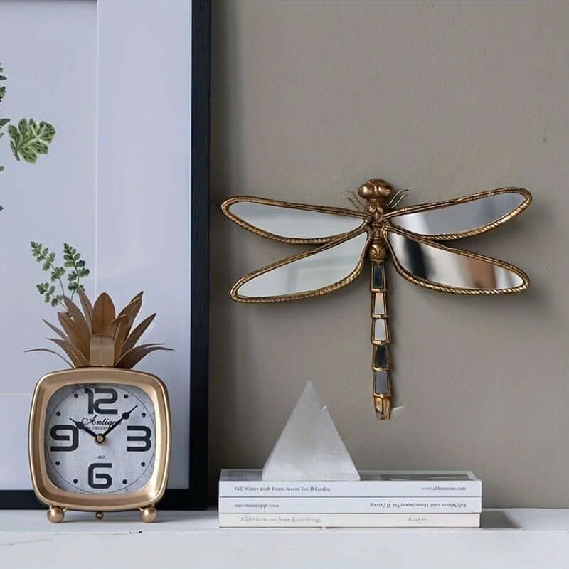 Decorative gold dragonfly wall art and clock on a shelf.